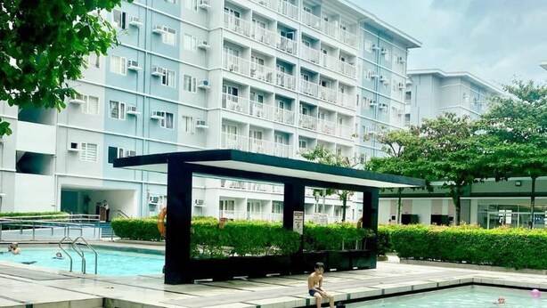A swimming pool area with a modern building in the background. - Aesthetic Cozy Stay with PS4, Netflix & Coffee Nook - Elena Suites Staycation (Quezon City)