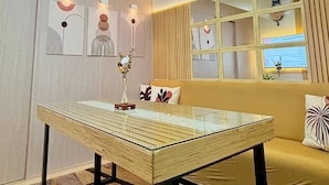 A modern room with a glass-top table, a sofa with patterned cushions, and a window with a view. - Aesthetic Cozy Stay with PS4, Netflix & Coffee Nook - Elena Suites Staycation (Quezon City)
