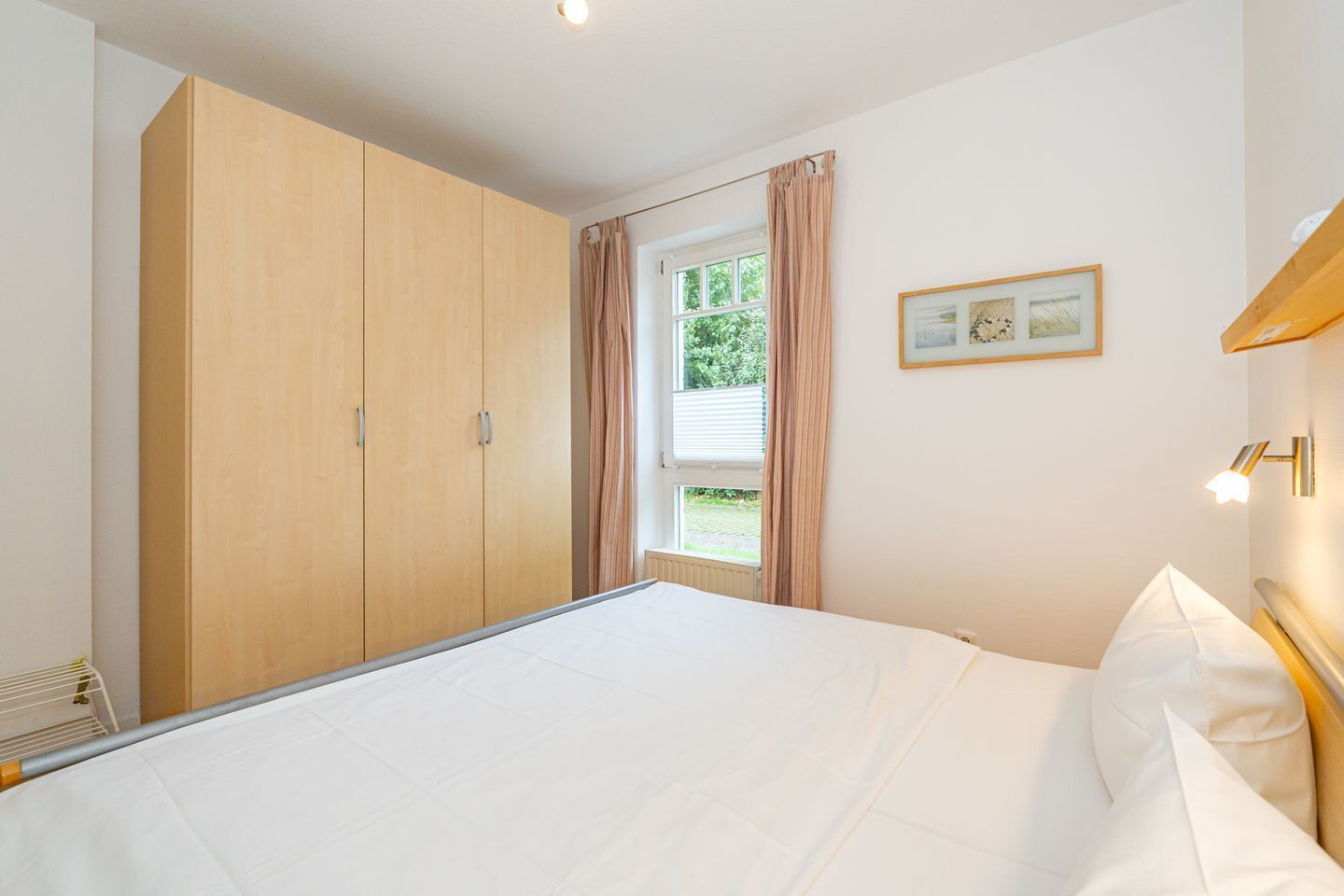 Een slaapkamer met een groot bed, een kledingkast, een raam met gordijnen en een lijst met een foto aan de muur.