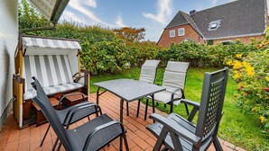 An outdoor patio with a table and four chairs, a striped sofa, and a grill. - Haus Conwind Apartment 1 - Comfortable vacation apartment Syltkoje with terrace and (Sylt-Ost)