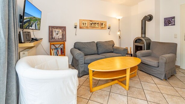 A living room with a grey sofa, a white armchair, a wooden coffee table, a TV, a fireplace, and a bookshelf with books. - Haus Conwind Apartment 1 - Comfortable vacation apartment Syltkoje with terrace and (Sylt-Ost)