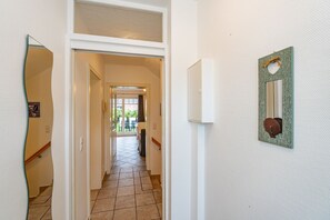 Un pasillo con suelo de baldosas, una puerta que da a un balcón y una lámpara fijada a la pared.