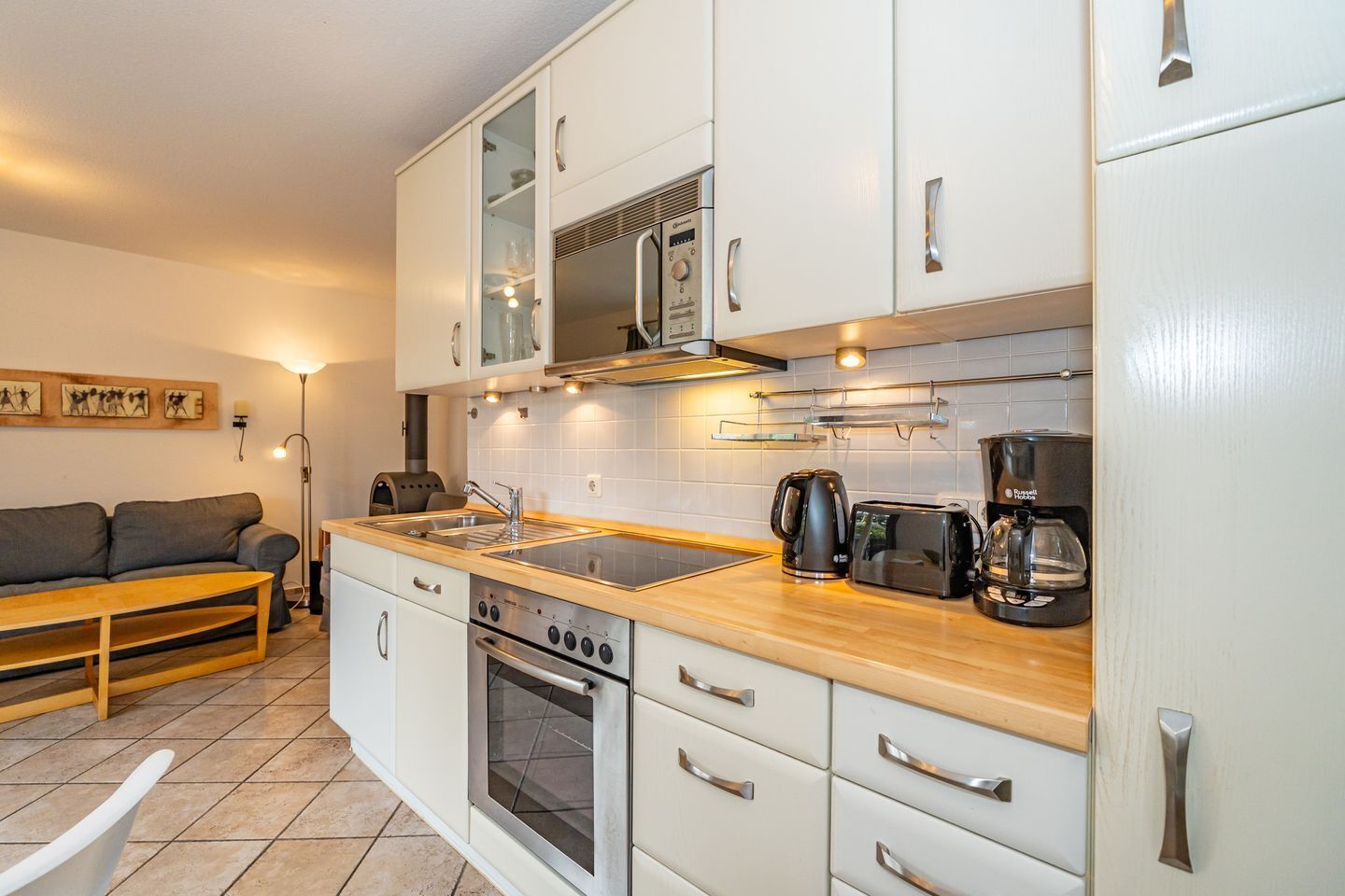 Eine kleine Küche mit weißen Schränken, einer Holz Arbeitsplatte, einem Einbauofen, einer Kaffeemaschine und einem Toaster.