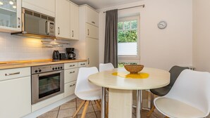 A modern kitchen with white cabinets, a stainless steel oven, and a round table with white chairs. - Haus Conwind Apartment 1 - Comfortable vacation apartment Syltkoje with terrace and (Sylt-Ost)