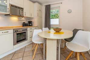 Una cocina moderna con armarios blancos, un horno de acero inoxidable y una mesa redonda con sillas blancas.