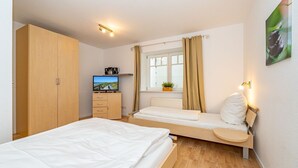 A bedroom with a bed, a TV, a wardrobe, a window with curtains, and a bedside table with a lamp. - Haus Conwind Apartment 1 - Comfortable vacation apartment Syltkoje with terrace and (Sylt-Ost)