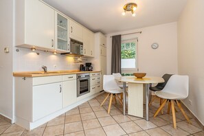 A modern kitchen with white cabinets, a wooden countertop, a built-in oven, and a dining area with a round table and two chairs.