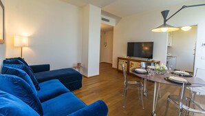 A modern living room with a blue sofa set, a dining table with chairs, a TV, and a lamp. - SkyAttic - 801 by Houset (Milano)