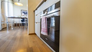 A modern kitchen with stainless steel appliances, a wooden floor, and a dining area in the background. - SkyAttic - 801 by Houset (Milano)