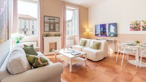 A modern living room with a white sofa, a coffee table, a TV, and a dining area with chairs and a table.