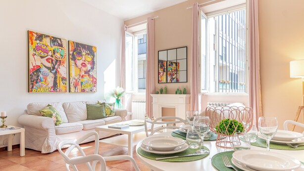 A well-lit living room with a dining area, a sofa, a fireplace, and artwork on the walls.