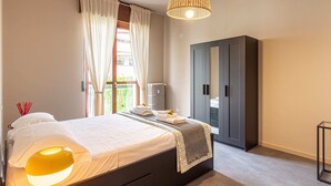 A bedroom with a bed, a wardrobe, a radiator, and a window with curtains. - Urban House - 301 by Houset (Monza)