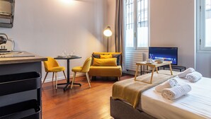Habitación de hotel con cama, escritorio, silla, televisión y ventana con cortinas.