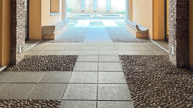 Un corredor abovedado con paredes de piedra y suelo de baldosas, que conduce a una zona de piscina.