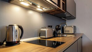 Una cocina moderna con tetera de acero inoxidable, tostadora y cafetera sobre una encimera de madera.