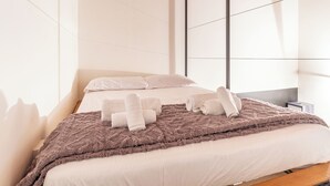 A modern hotel room with a large bed, a fluffy brown blanket, and neatly folded towels.