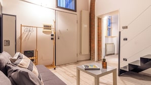 A modern hotel room with a bed, a table with a magazine, a coat rack, a radiator, and a staircase.
