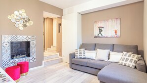 A living room with a grey sofa, red ottomans, a fireplace with patterned tiles, a wall art piece, and a staircase leading to another room. - Isolino Bridge Apartment by Houset (Monza)