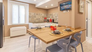 A modern kitchen with a wooden table set for dining, a coffee machine, and a TV mounted on the wall. - Isolino Bridge Apartment by Houset (Monza)
