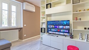 A modern living room with a flat-screen TV, white shelving, and a red ottoman. - Isolino Bridge Apartment by Houset (Monza)