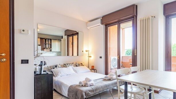 A modern bedroom with a bed, bedside table, and a dining table with chairs. - Cielo C18 by Houset - Two Bedroom Apartment, Sleeps 5 (Cinisello Balsamo)