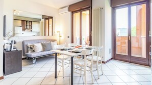 A modern kitchen with white cabinets, a dining table set for four, and a sofa in the living area. - Cielo C18 by Houset - Two Bedroom Apartment, Sleeps 5 (Cinisello Balsamo)