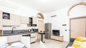 A modern kitchen with a dining area, a TV, and a sofa with a yellow pillow. - Cascina Fedeli by Houset (Monza)
