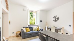 A modern kitchen with a dining area, a grey sofa with yellow cushions, and a large window with a view of greenery. - Cascina Fedeli by Houset (Monza)