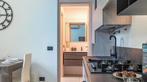A modern kitchen with a built-in stove, a dining area with a white chair, and a wall clock. - Cascina Fedeli by Houset (Monza)