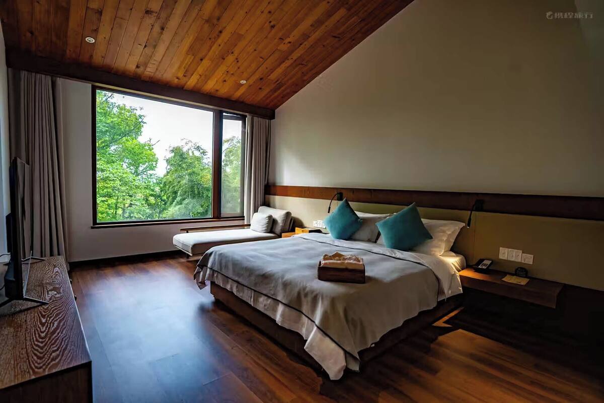 Un dormitorio con un ventanal grande, techo de madera y una cama con almohadas.