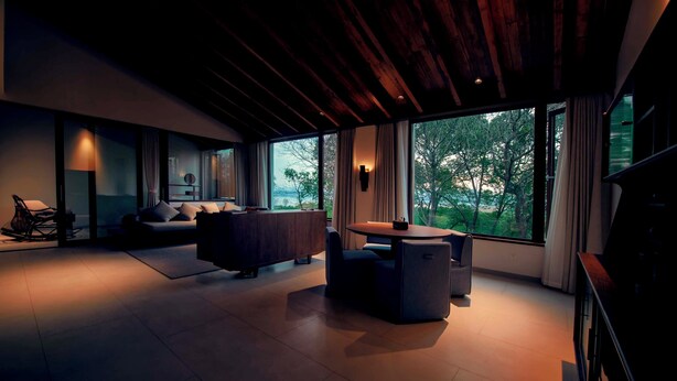 Una sala moderna con sofá, mesa de comedor y vista a árboles a través de amplias ventanas.