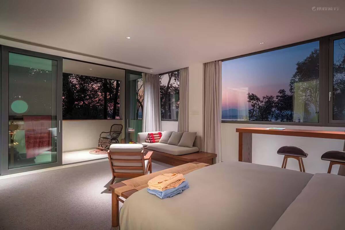 Una habitación de hotel moderna con una cama grande, un escritorio y un área de descanso con vistas a los cerezos en flor.
