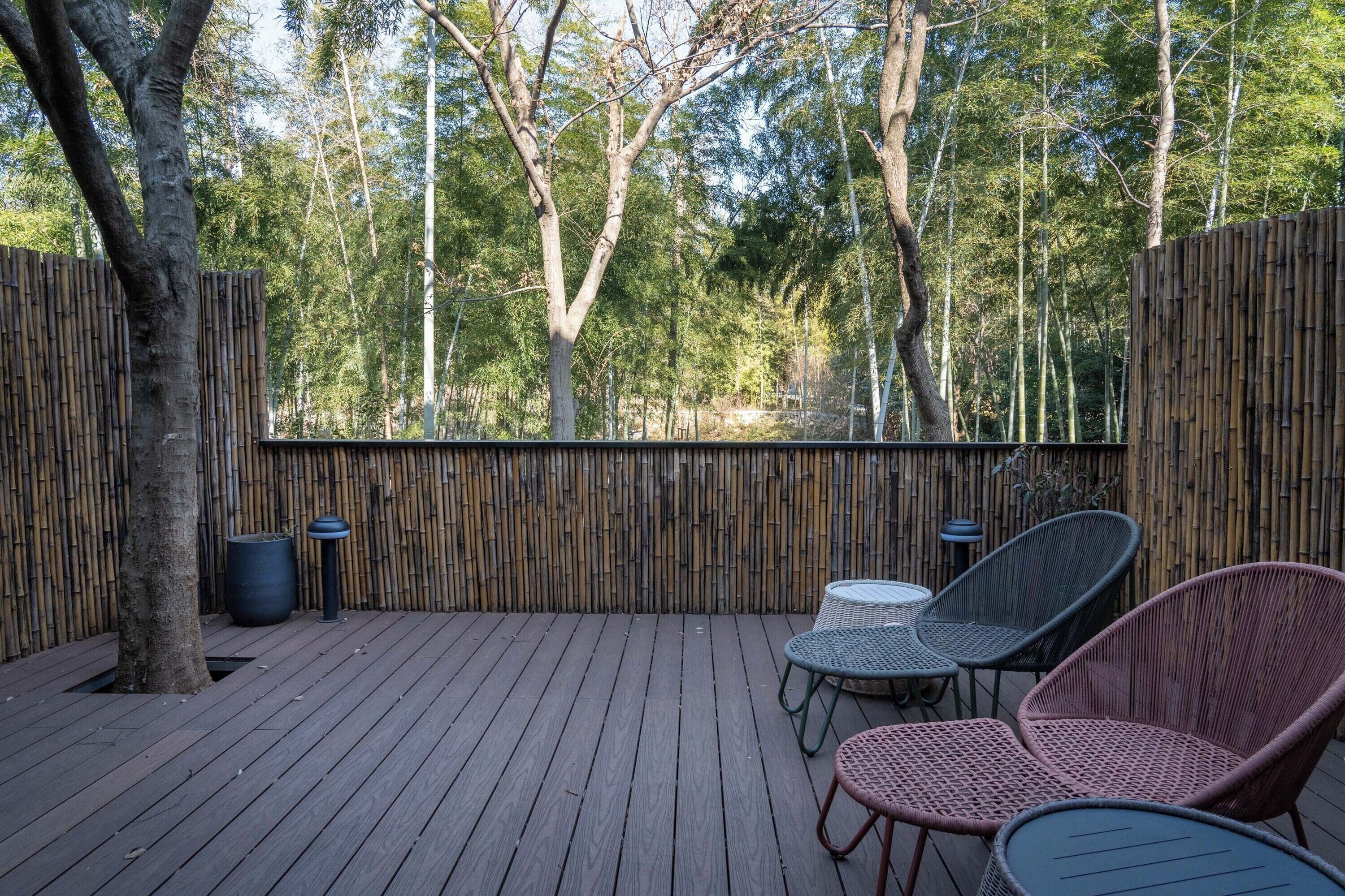 Eine Holzterrasse mit Korbstühlen und einem Tisch, umgeben von Bambuszaun und Bäumen.