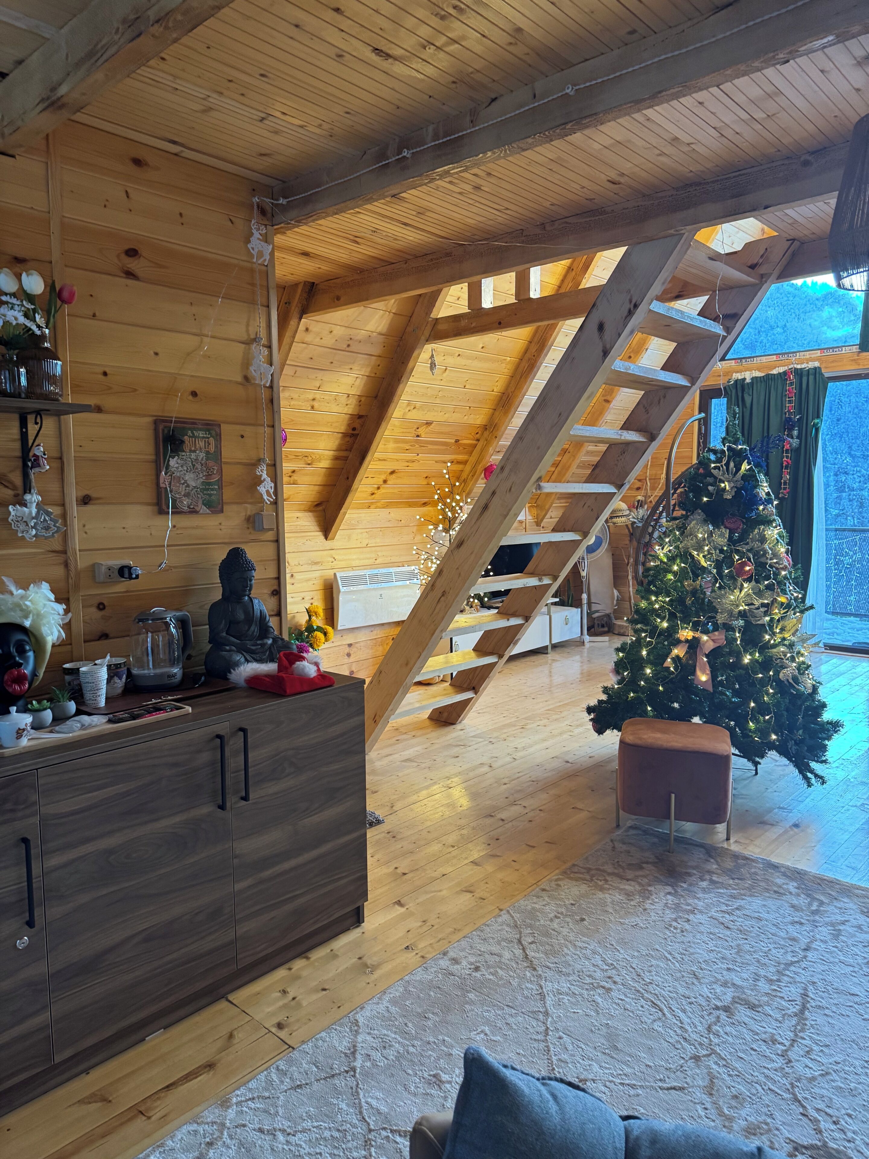 Interior de uma cabana de madeira com escada, árvore de Natal e área de jantar.