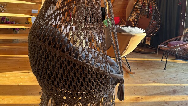 A macrame hanging chair in a wooden cabin with a sloped ceiling and a view of the sky. - Villa Cottage Merisi (Keda)