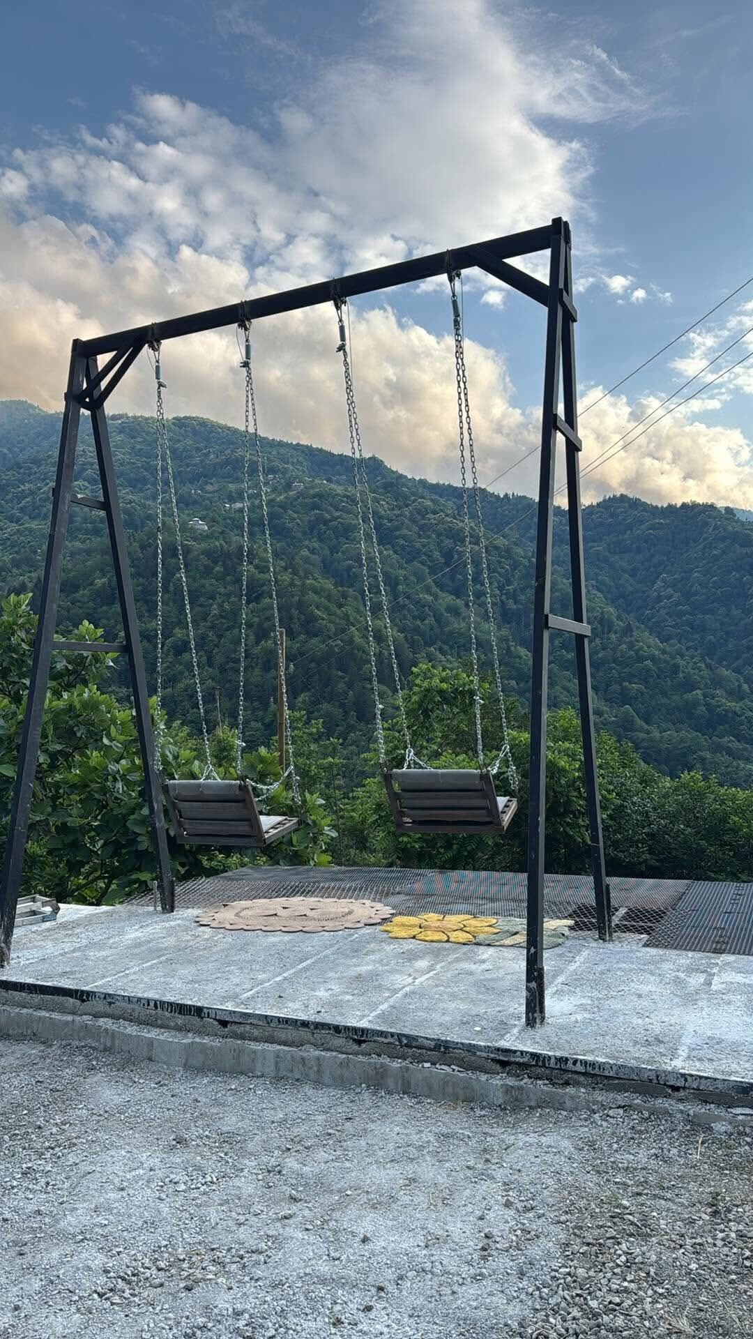 Un columpio con dos asientos, una cerca de metal y vistas a una cadena montañosa boscosa.