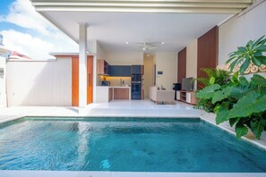 A modern indoor pool area with a kitchen and living space in the background. - Villa Kamandari (Seminyak)