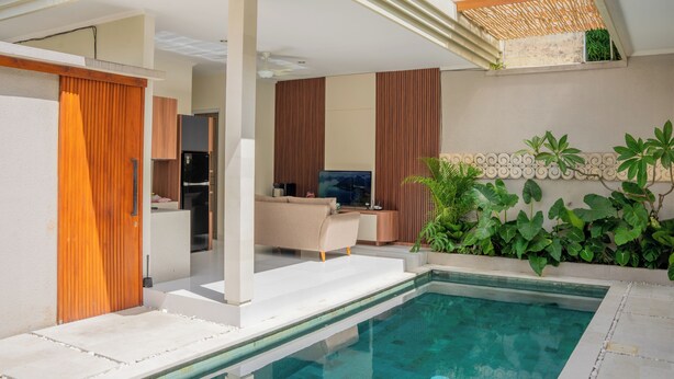 Un espace piscine intérieur moderne offrant une vue dégagée sur le salon, avec un canapé et un téléviseur.