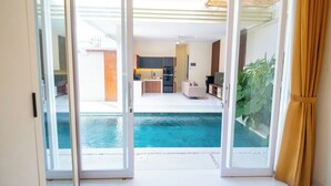 Une porte coulissante s’ouvrant sur un espace de vie comprenant une piscine, une cuisine et un coin repas.