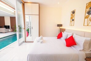 A hotel room with a bed, a pool view, and a sliding door leading to a balcony. - Villa Kamandari (Seminyak)