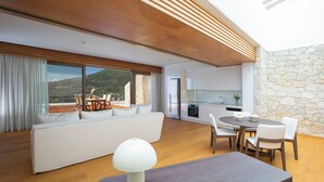 Ein modernes Wohnzimmer mit einer Couch, einem Esstisch und Stühlen. Im Hintergrund ist eine Küche zu sehen.