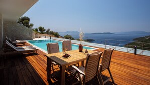 Eine Holzterrasse mit Pool, Sitzgelegenheit und Meerblick.