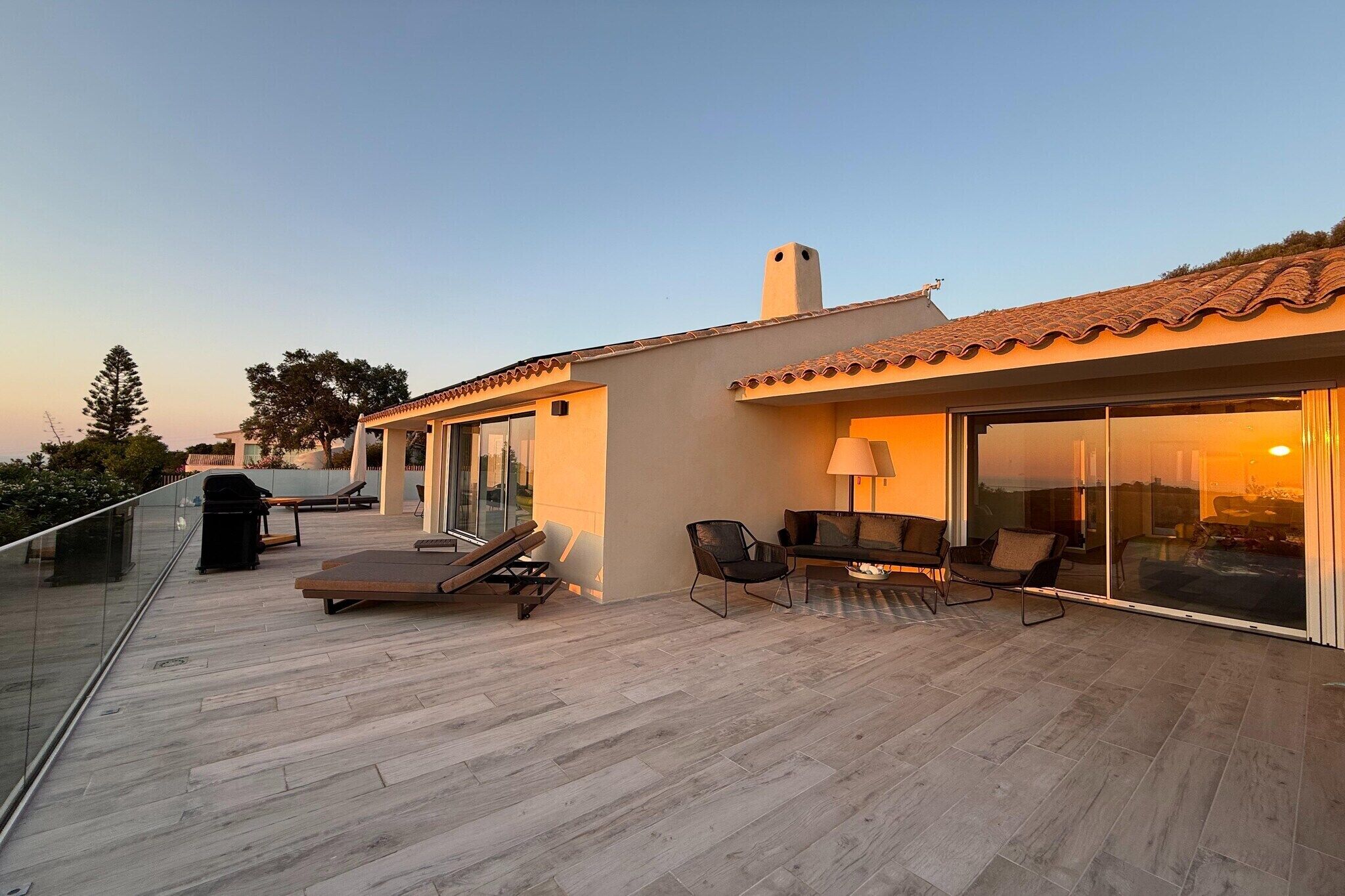 A rooftop terrace with a glass balustrade, lounge chairs, and a dining area with a table and chairs.