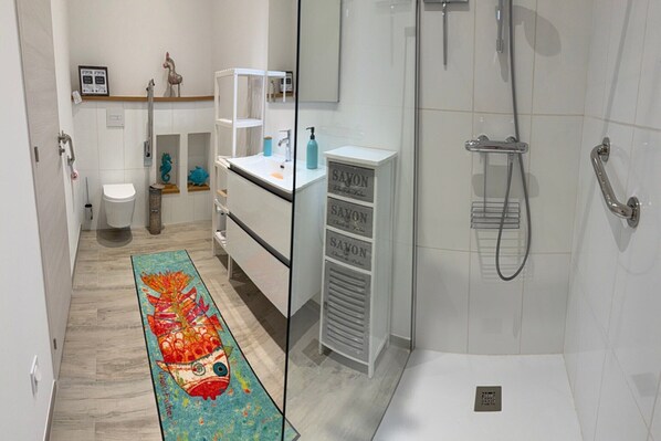 Une salle de bain moderne avec une douche à l’italienne en verre, un lavabo blanc doté d’un distributeur de savon et un tapis coloré.