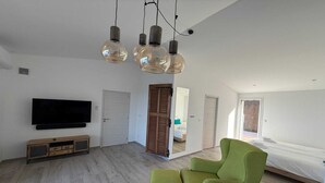 A modern living room with a flat-screen TV, a wooden cabinet, a green armchair, and a ceiling light fixture. - Vacation home near Porto Vecchio (Porto-Vecchio)
