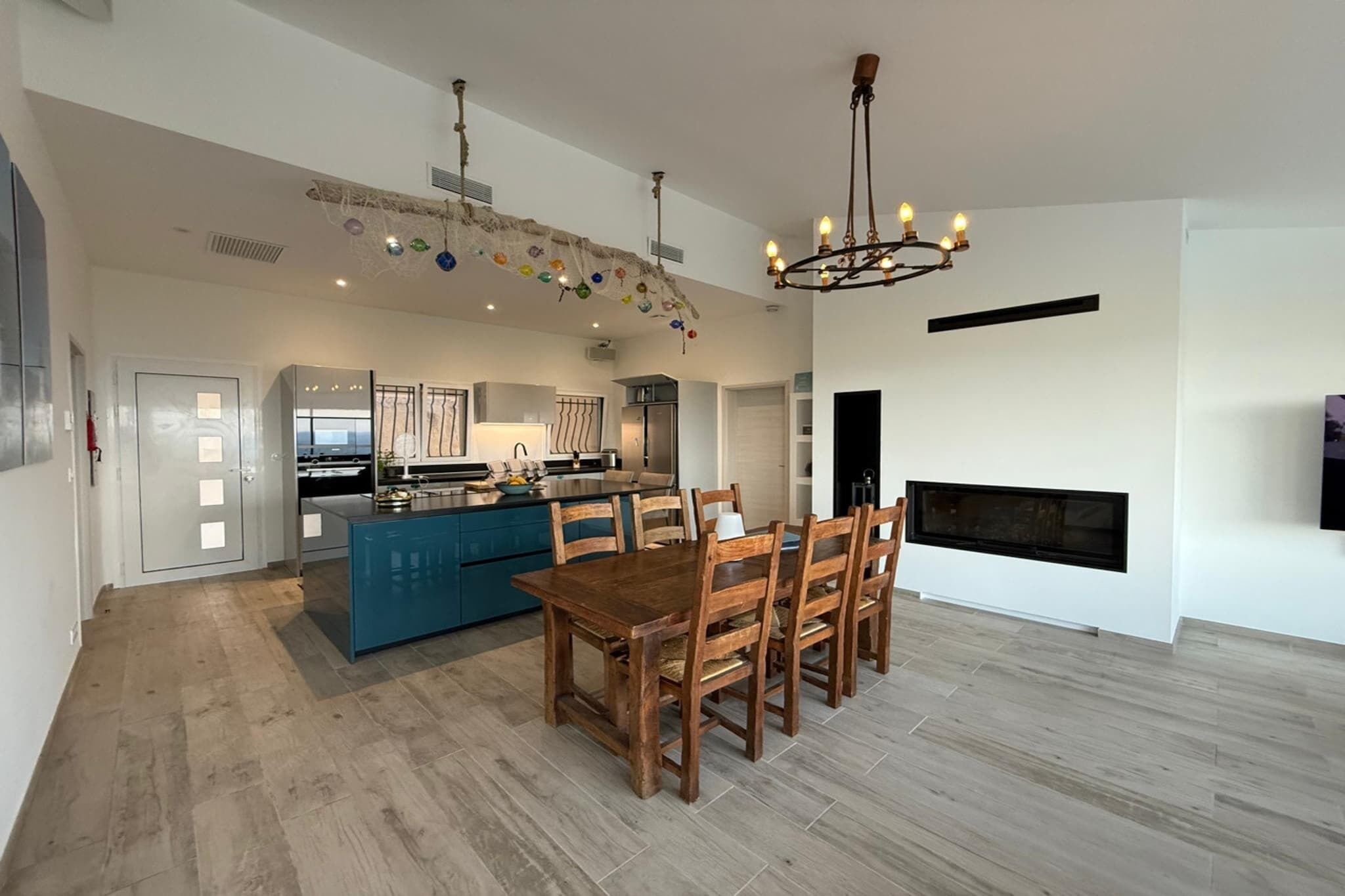 A modern kitchen with a central island, a dining area with wooden chairs, and a fireplace.
