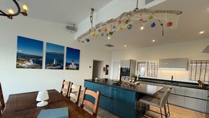 A modern kitchen with a central island, blue cabinets, and a dining area with a wooden table and chairs. - Vacation home near Porto Vecchio (Porto-Vecchio)