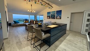 A modern kitchen with a large island, bar stools, and a view of the city. - Vacation home near Porto Vecchio (Porto-Vecchio)