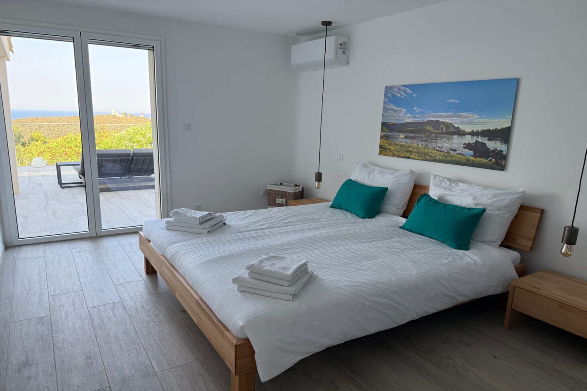 Une chambre moderne avec un grand lit, deux tables de chevet, un climatiseur fixé au mur et une porte-fenêtre coulissante donnant sur un espace extérieur.