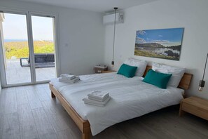 A modern bedroom with a large bed, two nightstands, a wall-mounted air conditioner, and a sliding glass door leading to an outdoor area.